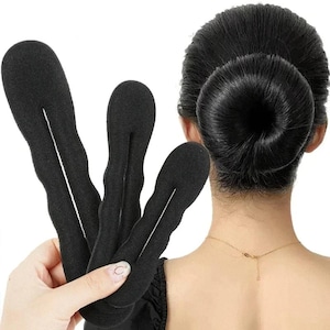 May include: Three black foam hair bun makers are held in front of a person's head with a neatly styled bun. The bun makers have a slit down the center and are designed to create a perfect bun hairstyle. The person is wearing a black top.