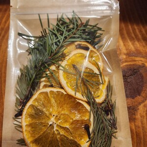 Puede incluir: Una bolsa de plástico transparente llena de rodajas de naranja secas, agujas de pino y clavos. Las rodajas de naranja son de un color amarillo intenso y las agujas de pino son de un verde oscuro.