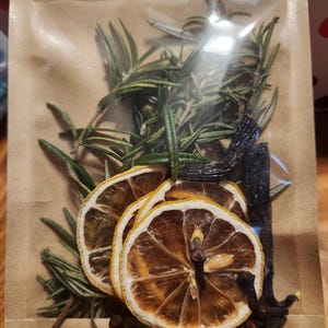 May include: A clear plastic bag filled with dried lemon slices, rosemary sprigs, vanilla beans, and cloves. The bag is on a brown paper background.