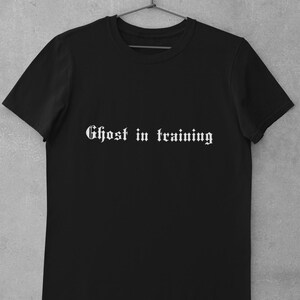 May include: Black t-shirt with white text that reads "Ghost in training" in a gothic font.