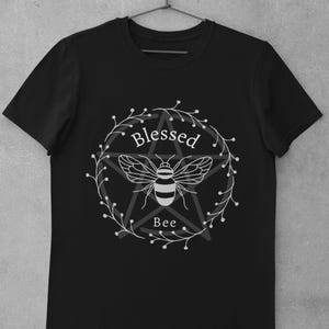 May include: Black t-shirt with a white graphic of a bee inside a pentagram with the words "Blessed Bee" around it.