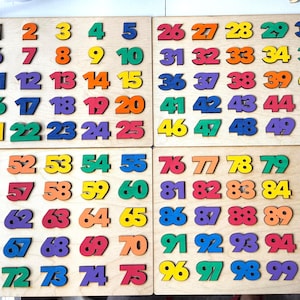May include: Wooden number puzzle boards with numbers 1-100 in various colors. Each number is a separate piece that fits into a corresponding slot on the wooden board. The numbers are in a variety of colors, including red, orange, yellow, green, blue, and purple.