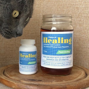 May include: A gray cat looks curiously at two bottles of "Potion of Healing" liquid cure. The bottles are on a wooden tray. The larger bottle is a glass jar with a brown liquid inside. The smaller bottle is white with a blue label. The text on the label reads "Potion of Healing" and "Fast-Acting".