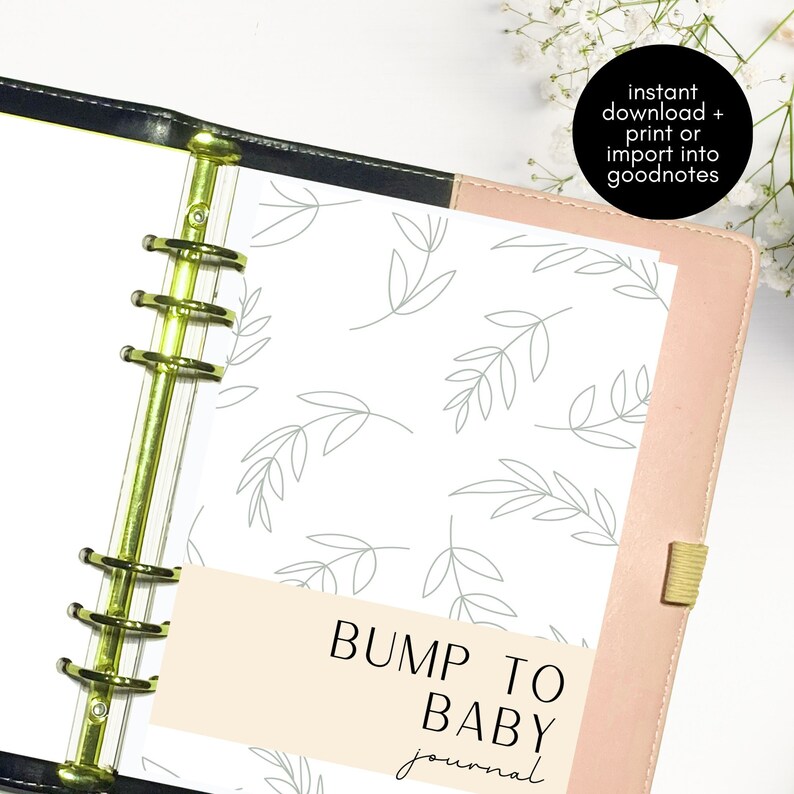 Op de afbeelding: Een roze en zwarte map met een witte pagina erin. De pagina heeft een grijs bladerenpatroon en de tekst "BUMP TO BABY journal" in zwart.