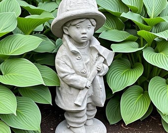 Pode incluir: Uma estátua de jardim em pedra cinzenta de uma criança vestida com uniforme de bombeiro, incluindo capacete e casaco comprido, segurando um pequeno machado. A figura assenta numa base circular e apresenta detalhes esculpidos na roupa.