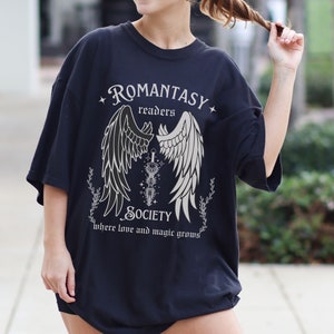 Puede incluir: Camiseta negra con un dise&ntilde;o gr&aacute;fico blanco que presenta un par de alas de &aacute;ngel, una espada y el texto "Romantasy Readers Society where love and magic grows".