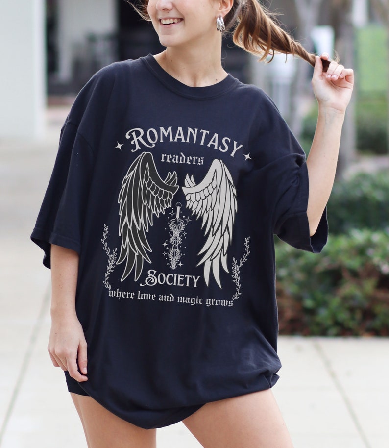 Puede incluir: Camiseta negra con un dise&ntilde;o gr&aacute;fico blanco que presenta un par de alas de &aacute;ngel, una espada y el texto "Romantasy Readers Society where love and magic grows".