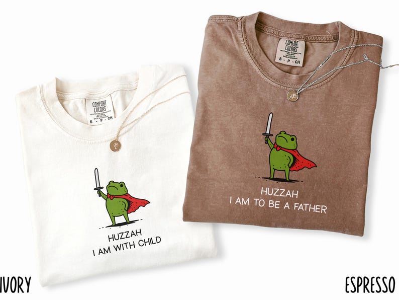 Puede incluir: Dos camisetas Comfort Colors, marfil y espresso, cada una con un dise&ntilde;o de rana de dibujos animados. La camiseta marfil dice "HUZZAH I AM WITH CHILD", y la camiseta espresso dice "HUZZAH I AM TO BE A FATHER".