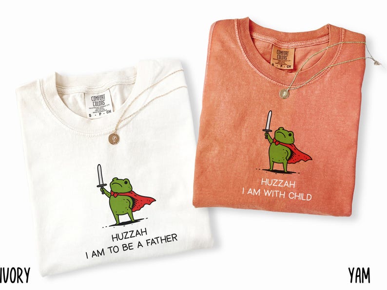 Puede incluir: Dos camisetas, una marfil y otra color &ntilde;ame, cada una con una rana de dibujos animados con capa y espada. La camiseta marfil dice "Huzzah I am to be a father". La camiseta color &ntilde;ame dice "Huzzah I am with child."