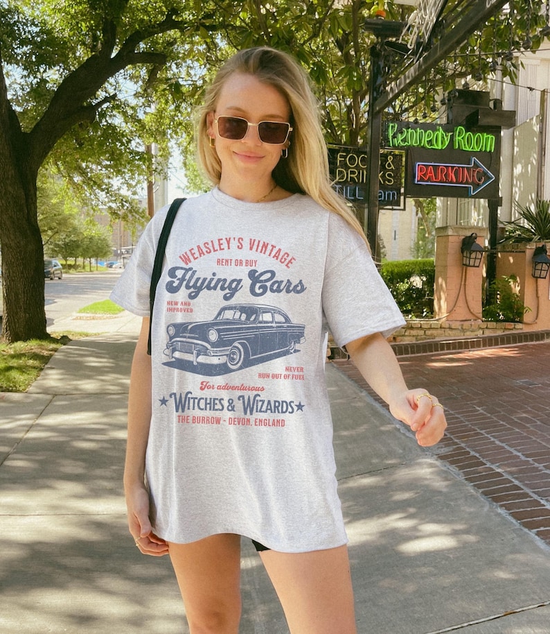 May include: A gray t-shirt with a vintage-style graphic of a car and the text "WEASLEY'S VINTAGE Flying Cars RENT OR BUY NEW AND IMPROVED RUN OUT OF FUEL For adventurous WITCHES & WIZARDS THE BURROW - DEVON, ENGLAND"