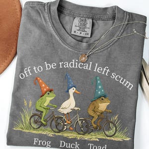 May include: Pepper-colored t-shirt with the phrase "off to be radical left scum" and illustrations of a frog, duck, and toad riding bicycles. The shirt also has the words "Frog Duck Toad" printed below the illustrations.