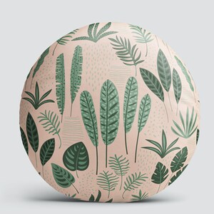 K&ouml;nnte beinhalten: Ein rundes Kissen mit rosa Hintergrund und einem sich wiederholenden Muster aus gr&uuml;nen Bl&auml;ttern. Die Bl&auml;tter sind in verschiedenen Formen und Gr&ouml;&szlig;en, darunter Palmbl&auml;tter, Farne und Monstera-Bl&auml;tter.