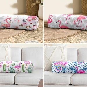 Puede incluir: Cuatro cojines cilíndricos decorativos con diseños de flamencos. Los cojines presentan varios patrones, incluyendo estampados florales, chevron y cactus, con flamencos rosas. Los cojines son cilíndricos y descansan sobre una superficie neutra y un sofá blanco.