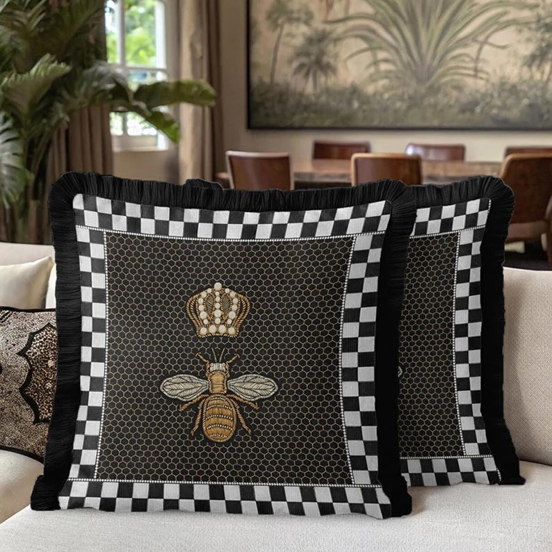 Puede incluir: Dos cojines decorativos con un borde a cuadros blanco y negro y flecos negros. El centro presenta un dise&ntilde;o de abeja y corona bordada en oro sobre un fondo de panal negro.