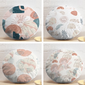 May include: Four round decorative throw pillows with various designs. One features a sun with a face, another has rainbows and suns, and the other two have Greek-inspired illustrations. The pillows have a white background with pink, teal, and brown accents.