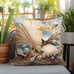 Puede incluir: Un coj&iacute;n cuadrado con un dise&ntilde;o detallado en relieve de varias conchas marinas en tonos dorado p&aacute;lido, crema y azul suave. La superficie muestra una disposici&oacute;n texturizada de conchas en forma de abanico, caracoles en espiral y detalles de coral.