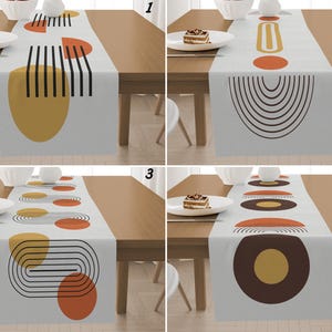 Puede incluir: Un conjunto de cuatro caminos de mesa blancos con patrones geométricos abstractos en tonos amarillo mostaza, naranja quemado y marrón oscuro. Los diseños incluyen semicírculos concéntricos, círculos sólidos y líneas paralelas repetidas.