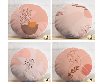 May include: Four round throw pillows with different abstract designs in shades of pink, brown, and white. The designs include a leaf, a bird, a hand holding a sprig of berries, and a hand holding a bird.