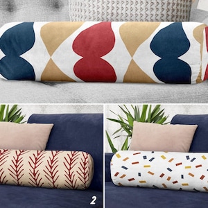 May include: Three decorative bolster cushions with different patterns. One has a geometric design in navy, red, and tan. Another features a repeating leaf pattern in red and beige. The third has a confetti-like pattern in various colours.