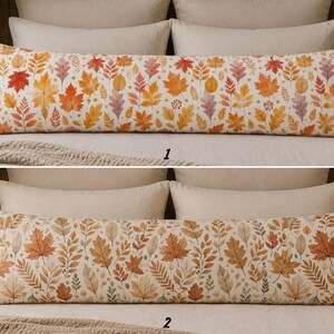 May include: Two long rectangular body pillows featuring autumn leaf patterns. The top pillow displays vibrant red, orange, and yellow maple and oak leaves on a cream background. The bottom pillow shows muted brown, tan, and soft green foliage.