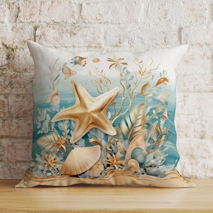 Puede incluir: Un coj&iacute;n cuadrado con un dise&ntilde;o estampado de una gran estrella de mar dorada, varias conchas marinas y algas doradas delicadas sobre un fondo degradado en azul y blanco. La imagen representa una escena submarina con texturas suaves.