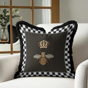Puede incluir: Coj&iacute;n decorativo cuadrado con un patr&oacute;n de panal de abeja negro y un dise&ntilde;o de abeja bordada en dorado, coronada con una corona. El coj&iacute;n tiene un borde a cuadros blanco y negro y flecos negros.