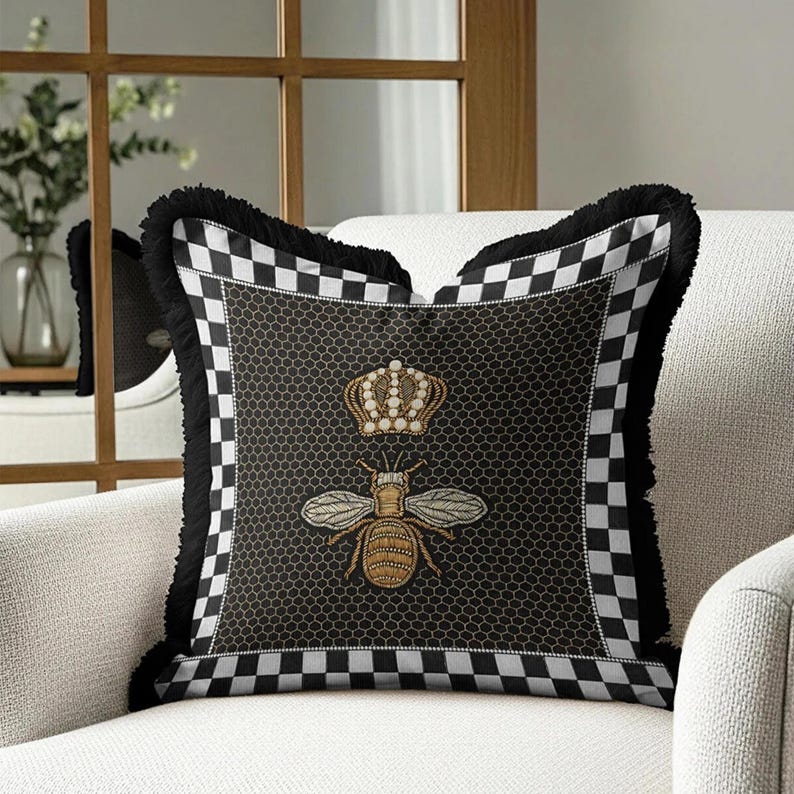 Puede incluir: Coj&iacute;n decorativo cuadrado con un patr&oacute;n de panal de abeja negro y un dise&ntilde;o de abeja bordada en dorado, coronada con una corona. El coj&iacute;n tiene un borde a cuadros blanco y negro y flecos negros.