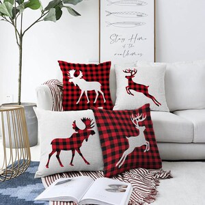 May include: A set of four square scatter cushions featuring alternating designs of red and black buffalo check patterns and solid off-white fabric. The cushions display silhouettes of moose and deer in contrasting colours across the front surfaces.