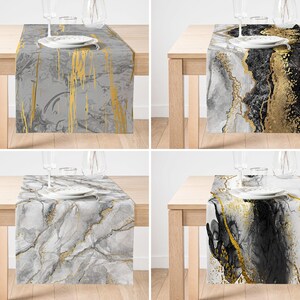 May include: Four table runners featuring a marble design with gold accents. The runners are displayed on wooden tables with glasses and plates on top.