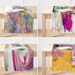 May include: Four different abstract table runners with colorful marbleized patterns. The runners are displayed on wooden tables with place settings.