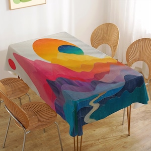 May include: A colorful abstract tablecloth with a rainbow design featuring a yellow sun and blue sky. The tablecloth is laid on a table with four wooden chairs.