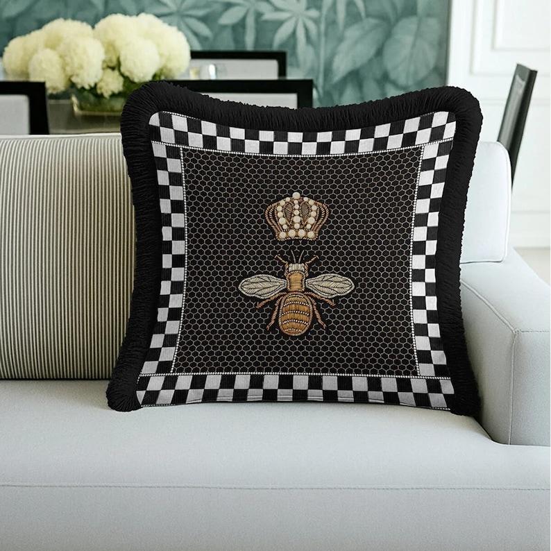 Puede incluir: Coj&iacute;n decorativo negro con dise&ntilde;o de abeja y corona. El coj&iacute;n presenta un fondo negro con un patr&oacute;n de panal, un bordado de abeja y corona, un borde a cuadros y una franja negra.