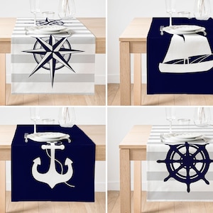 May include: Four table runners with nautical themes. The first runner features a white compass on a blue and white striped background. The second runner features a white sailboat on a blue background. The third runner features a white anchor on a blue background. The fourth runner features a white ship's wheel on a blue and white striped background.