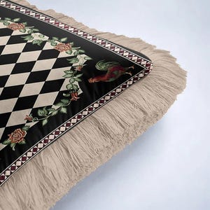 Puede incluir: Una alfombra decorativa con un patr&oacute;n de diamantes en negro y crema. El borde de la alfombra es negro con un dise&ntilde;o floral y un gallo. La alfombra tiene flecos beige.