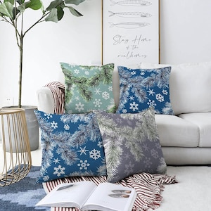 May include: Four square throw pillows featuring a winter theme with pine branch patterns and white snowflakes. The set includes one light green, two blue, and one gray pillow, each displaying a consistent botanical and seasonal design.