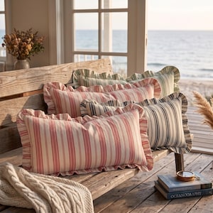 May include: Three rectangular throw pillows with ruffled edges, featuring vertical stripes in shades of red, blue, and green. The pillows are arranged on a wooden bench, showcasing a soft fabric texture and a classic striped pattern design.