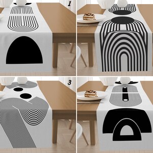 Könnte beinhalten: Weißer Tischläufer mit einem schwarzen geometrischen Design. Der Läufer zeigt verschiedene abstrakte Formen, darunter Bögen und Kreise. Der Läufer wird auf einem Holztisch präsentiert und zeigt eine moderne, minimalistische Ästhetik.