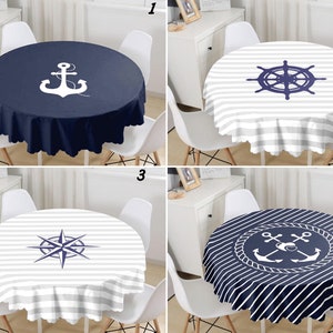 Op de afbeelding: Vier ronde tafelkleden met nautische thema's. Ontwerpen omvatten een anker, scheepsstuur, kompasroos en een anker in een touw cirkel. Elk tafelkleed ligt op een tafel met witte stoelen en een witte kast op de achtergrond.