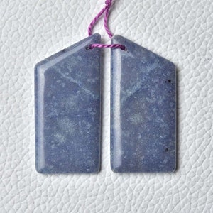 Könnte beinhalten: Ein Paar blaugrüne Edelsteinohrringe in rechteckiger Form mit leicht spitz zulaufender Oberseite. Die Ohrringe sind an einer rosa Schnur befestigt.