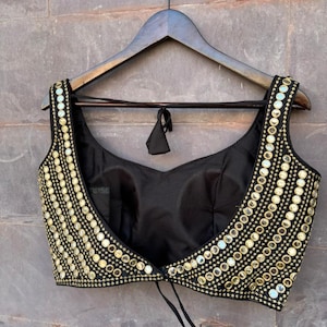 May include: A black sleeveless blouse featuring a wide scoop neckline and a cropped silhouette. The front panels are heavily embellished with rows of small, circular gold-toned mirrors and metallic gold embroidery, creating a dense, reflective pattern.