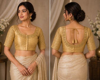 May include: A gold-coloured blouse with short sleeves and detailed embroidery. The blouse has a scoop neckline and a button-up front. The back of the blouse features a low scoop design with a tie closure. The blouse is worn with a matching gold-coloured skirt.