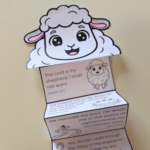 Puede incluir: Una manualidad de papel blanco y gris con una cabeza de oveja de dibujos animados y un cuerpo plegado. El cuerpo muestra vers&iacute;culos b&iacute;blicos del Salmo 23, incluyendo "Jehov&aacute; es mi pastor; nada me faltar&aacute;." Una manualidad encantadora y educativa.