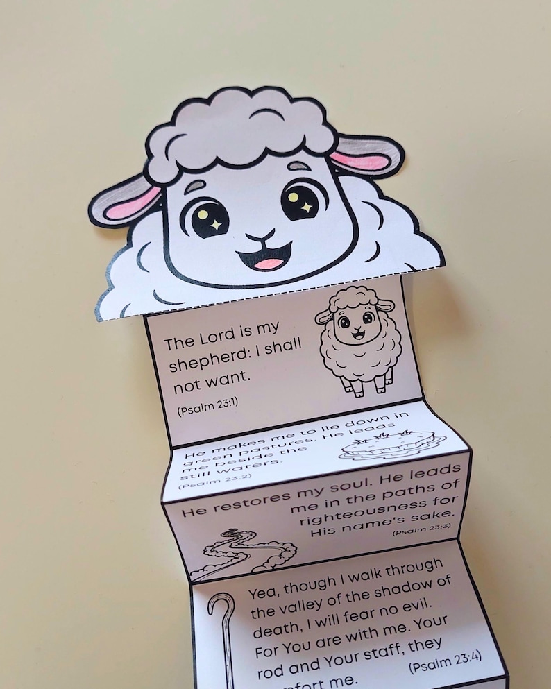 Puede incluir: Una manualidad de papel blanco y gris con una cabeza de oveja de dibujos animados y un cuerpo plegado. El cuerpo muestra vers&iacute;culos b&iacute;blicos del Salmo 23, incluyendo "Jehov&aacute; es mi pastor; nada me faltar&aacute;." Una manualidad encantadora y educativa.