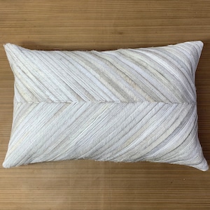 Könnte beinhalten: Ein weißes Lederkissen mit Chevron-Muster. Das Kissen ist rechteckig und hat eine weiche, strukturierte Oberfläche.