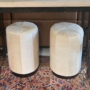 Könnte beinhalten: Ein schwarzer Metallkonsolentisch mit einer hellbeigen Marmorplatte. Zwei runde Hocker in Weiß und Beige stehen vor dem Tisch. Eine Bronzeskulptur eines Pferdes und Reiters steht auf dem Tisch.