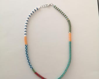 May include: A multi-colored beaded necklace with white, blue, orange, red, green, and silver beads. The necklace is made of small, round beads and has a silver clasp.