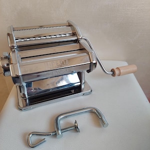 May include: A silver pasta maker with a wooden handle and a clamp. The machine is labeled "Imperia" and "Tipo Lusso 3+1+2".