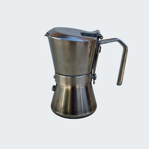 Pode incluir: Uma cafeteira de aço inoxidável para fogão com acabamento polido. A cafeteira possui uma base larga, uma câmara central, uma tampa articulada com um pequeno bico e uma alça angular resistente fixada na lateral do recipiente superior.