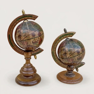 Pode incluir: Dois globos decorativos com cartografia de estilo vintage em tons terra suaves. Cada globo está montado num suporte de madeira castanho-escuro com um anel meridiano curvo. Os mapas exibem ilustrações históricas, incluindo navios e rosas dos ventos.