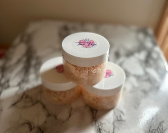 Puede incluir: Tres frascos blancos con tapas rosadas que contienen un exfoliante rosa claro y blanco. El frasco superior tiene una etiqueta rosa y blanca con el texto "Tori Faye" y una corona.